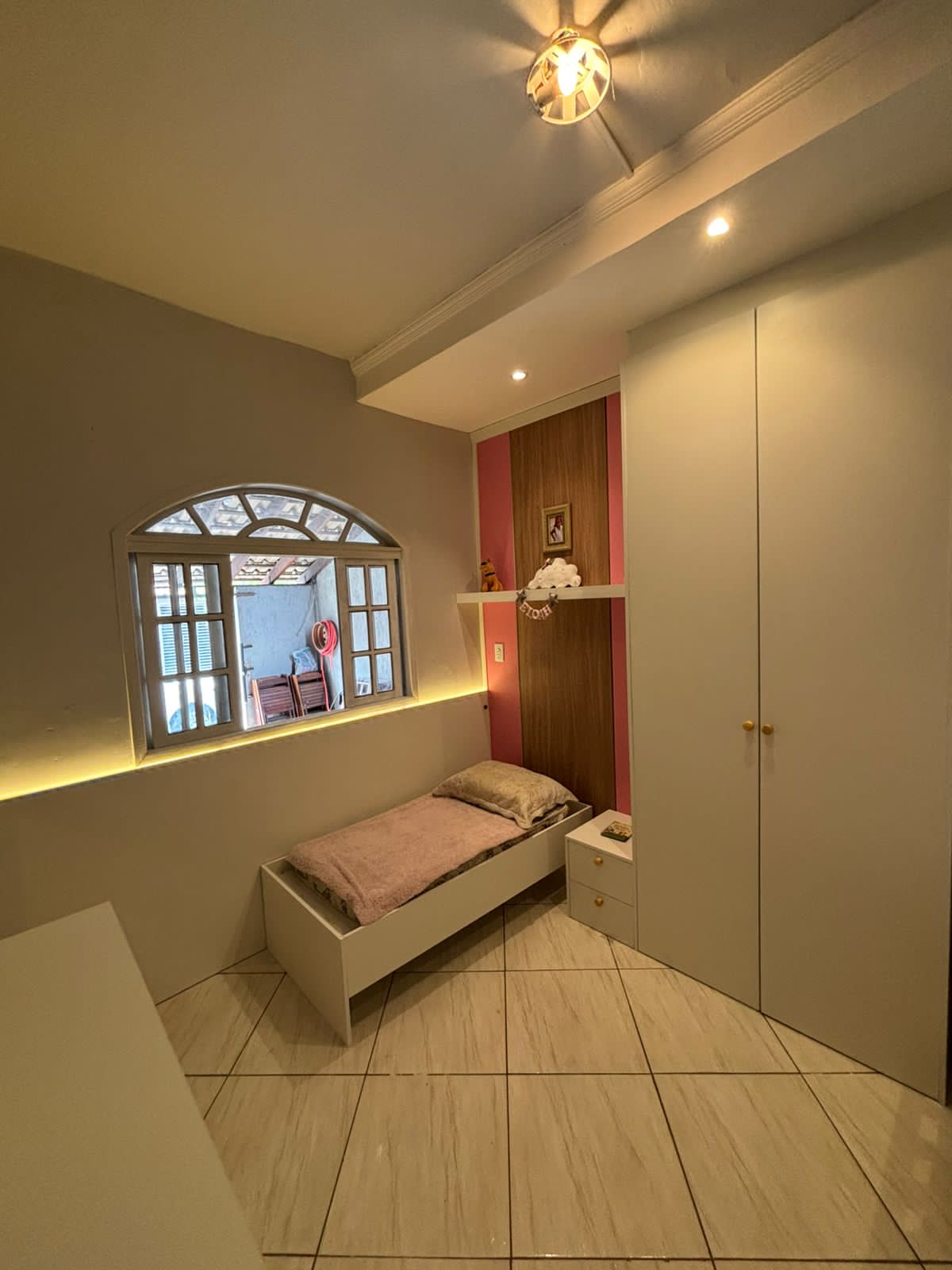 Quarto infantil feminino com cama de solteiro, guarda-roupa branco e parede rosa com painel amadeirado