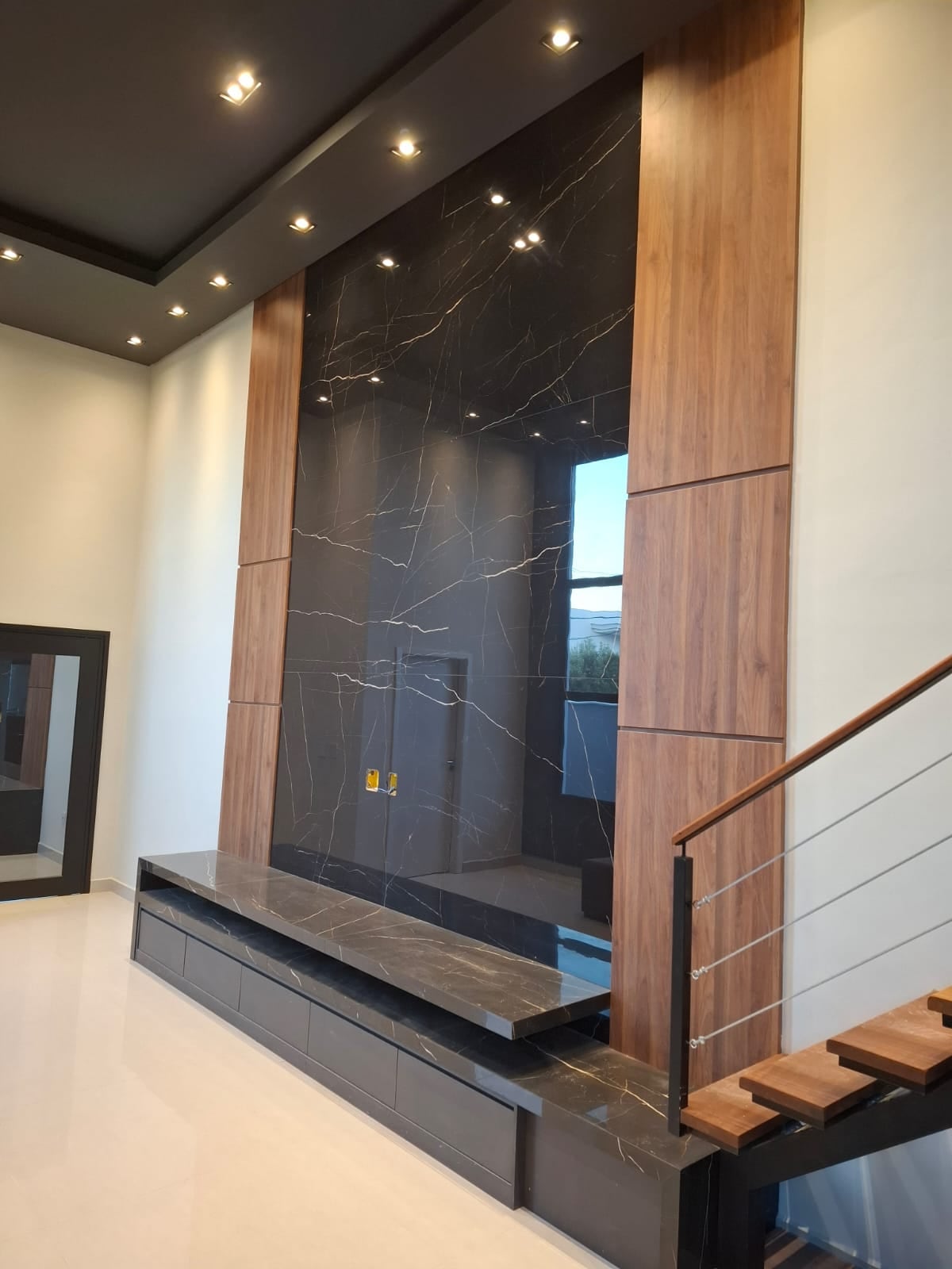 Painel de TV planejado em mármore preto com veios dourados ao lado da escada